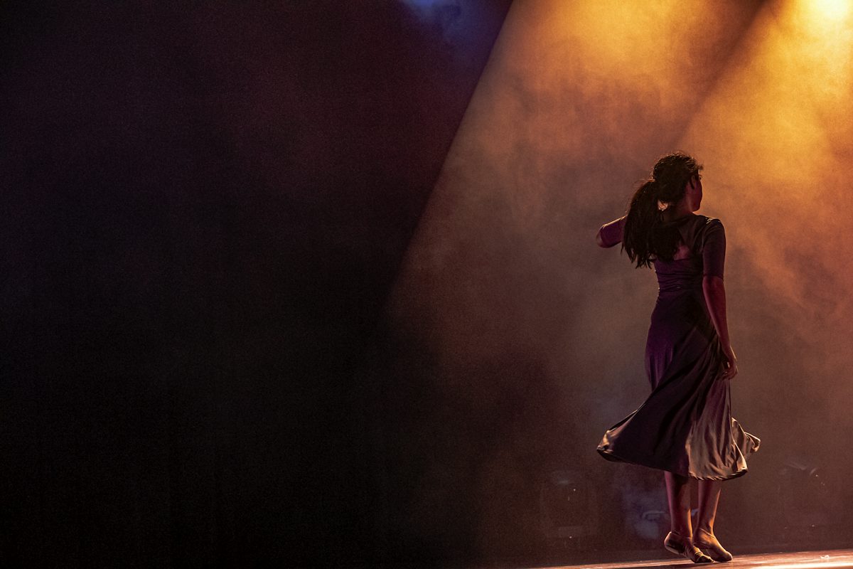 A woman in a dark dress dancing on stage under warm orange light — illustrative stock photo