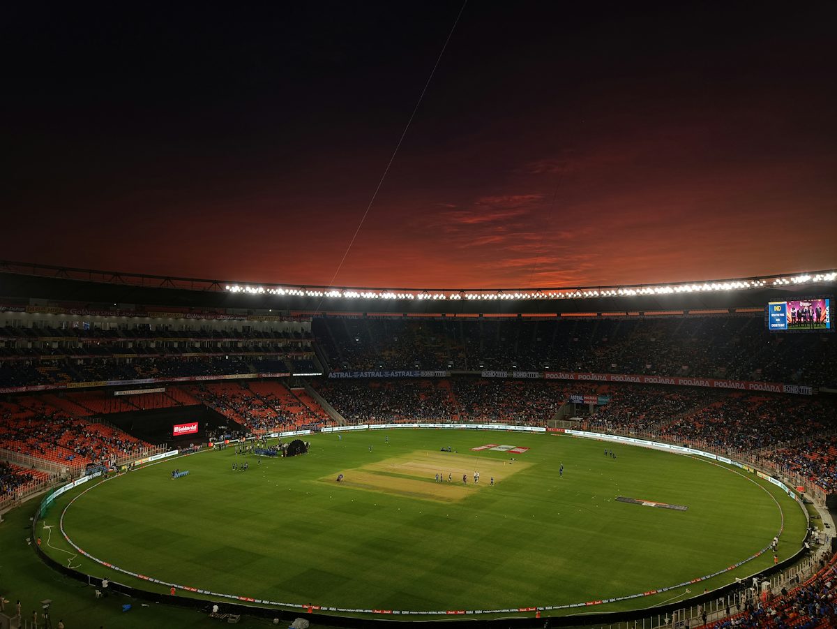 A cricket stadium with a green pitch under a dark red evening sky — illustrative stock photo