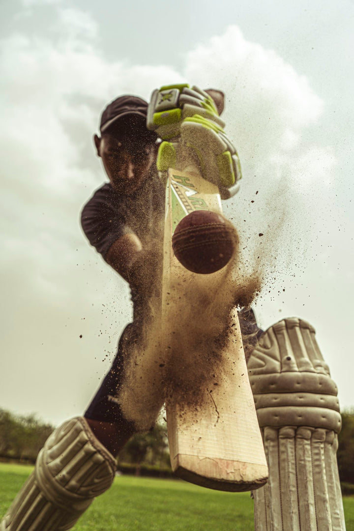 A cricket batsman hitting a ball with a wooden bat on a field — illustrative stock photo