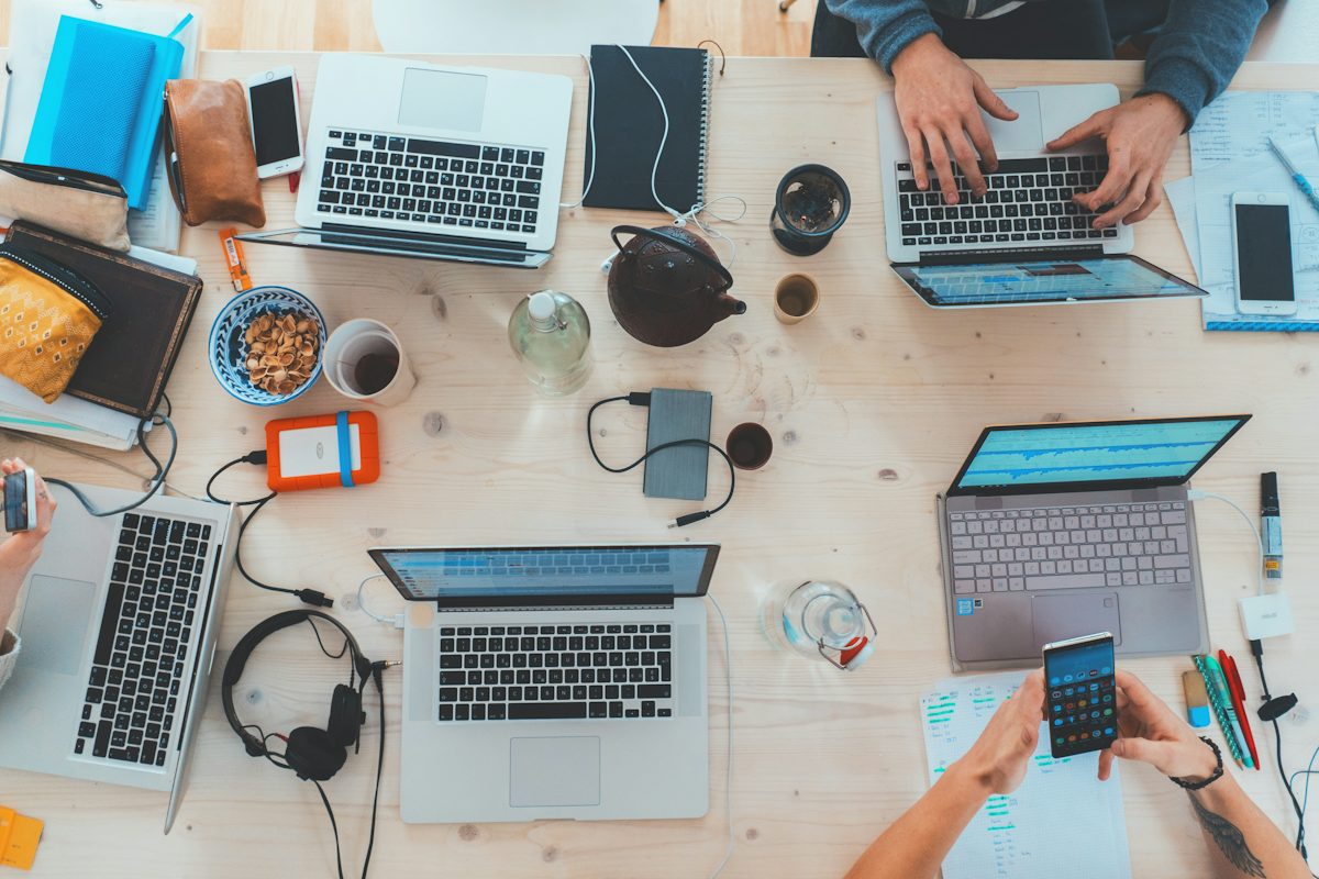 people sitting down near table with assorted laptop computers — illustrative stock photo