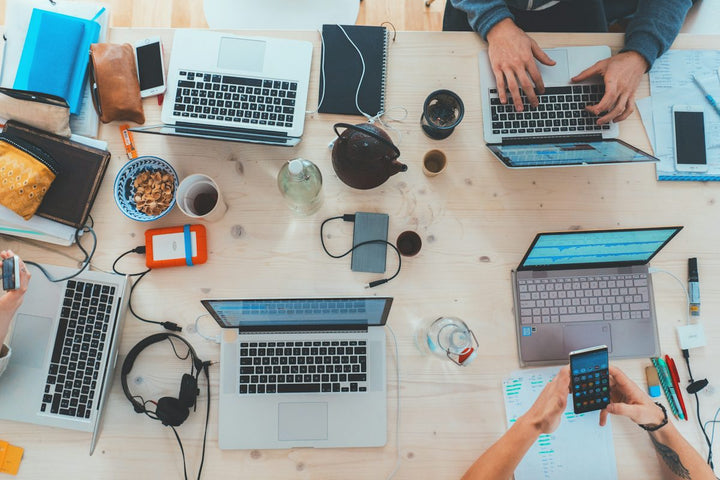 people sitting down near table with assorted laptop computers — illustrative stock photo